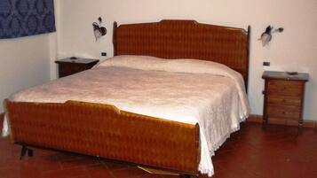 A single bed with a wooden headboard and footboard, flanked by two nightstands with lamps. The room has a tiled floor and plain walls.