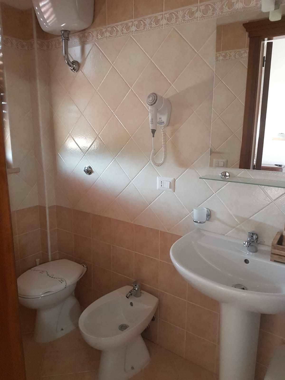 A bathroom with a pedestal sink, a bidet, and a hairdryer mounted on the wall.