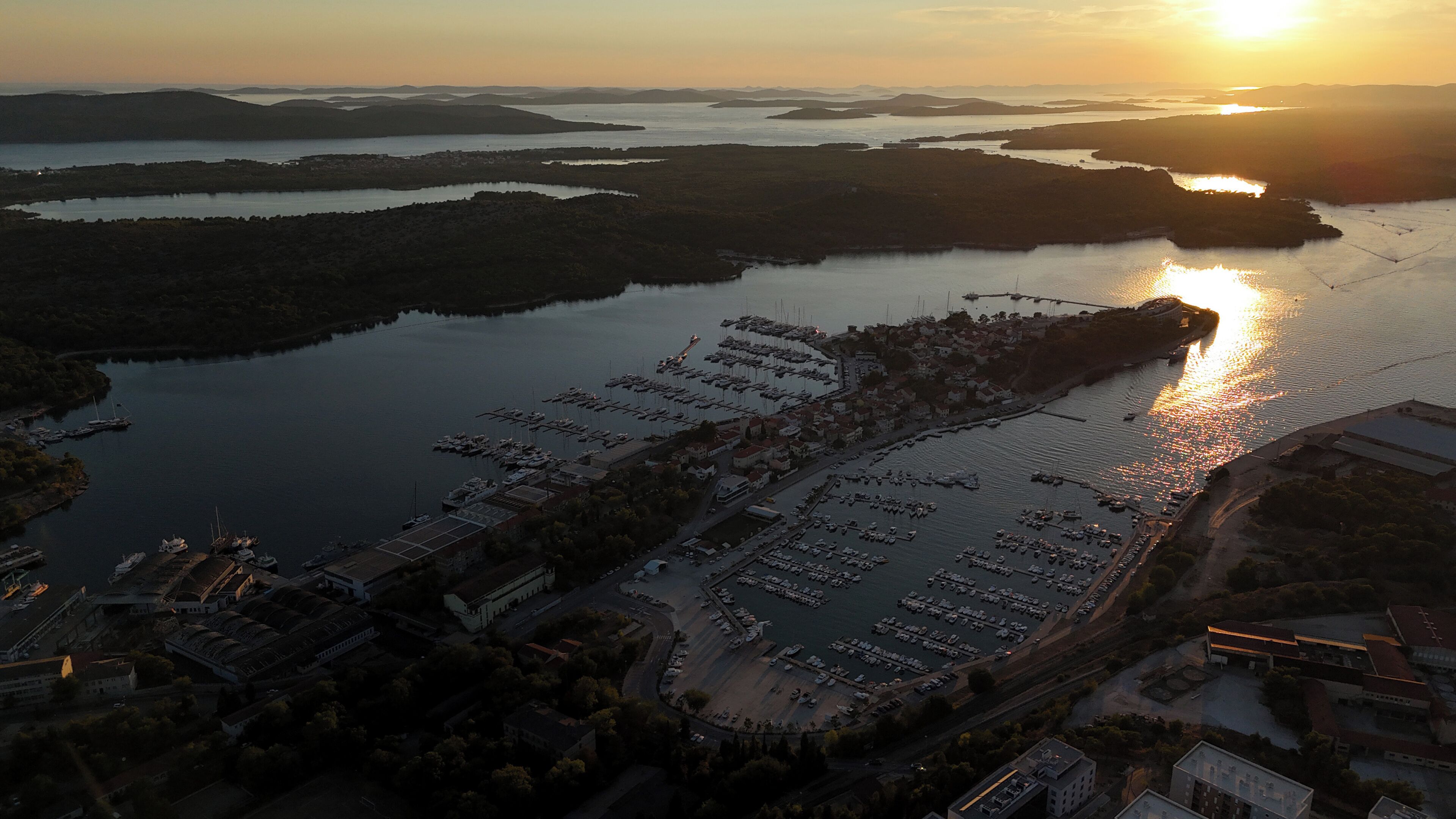 Vista aérea de un puerto deportivo con barcos amarrados, rodeado de agua y tierra.