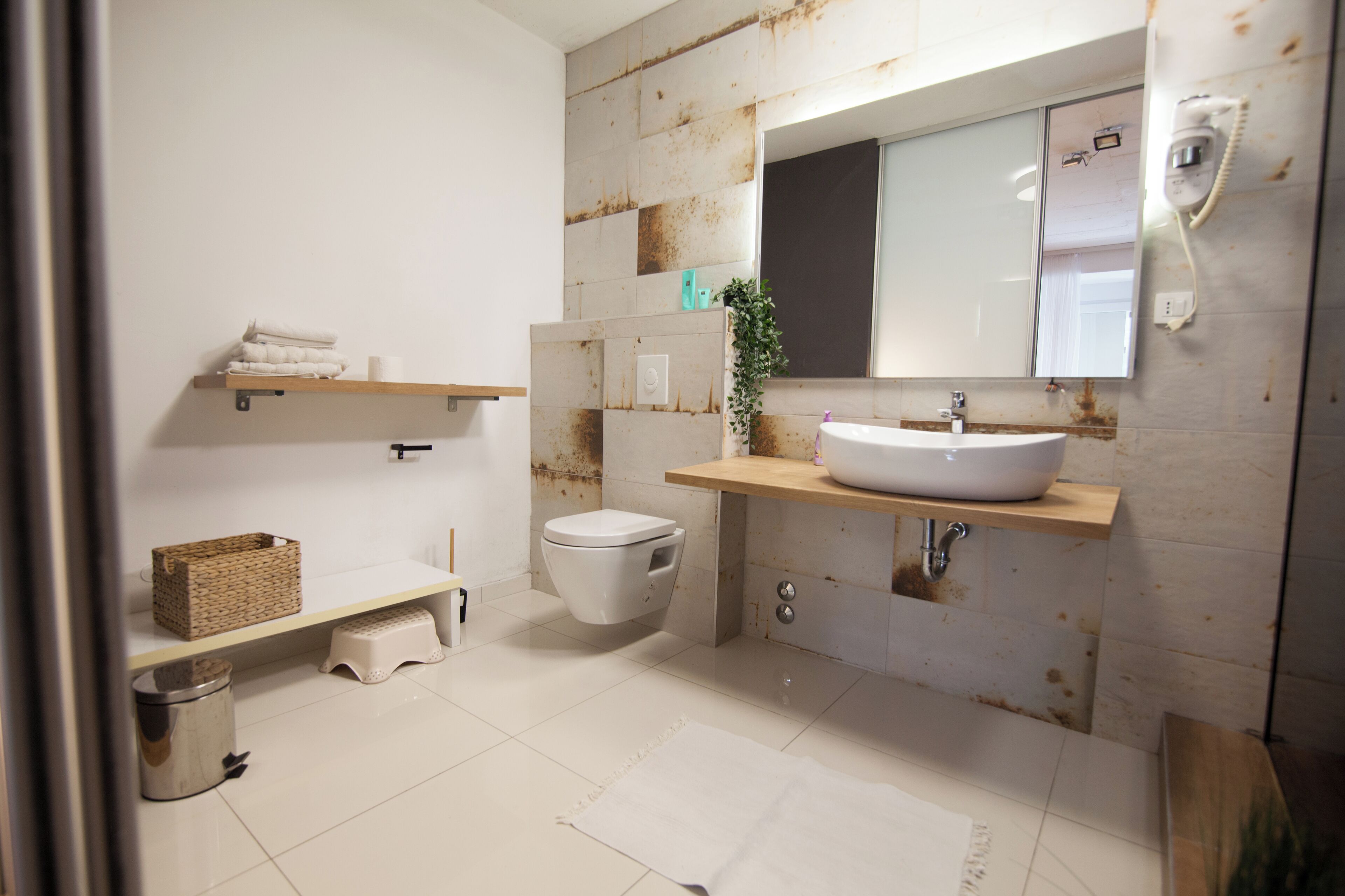 Une salle de bain avec un lavabo blanc, des toilettes et un miroir. On y trouve une étagère avec des serviettes et un panier.