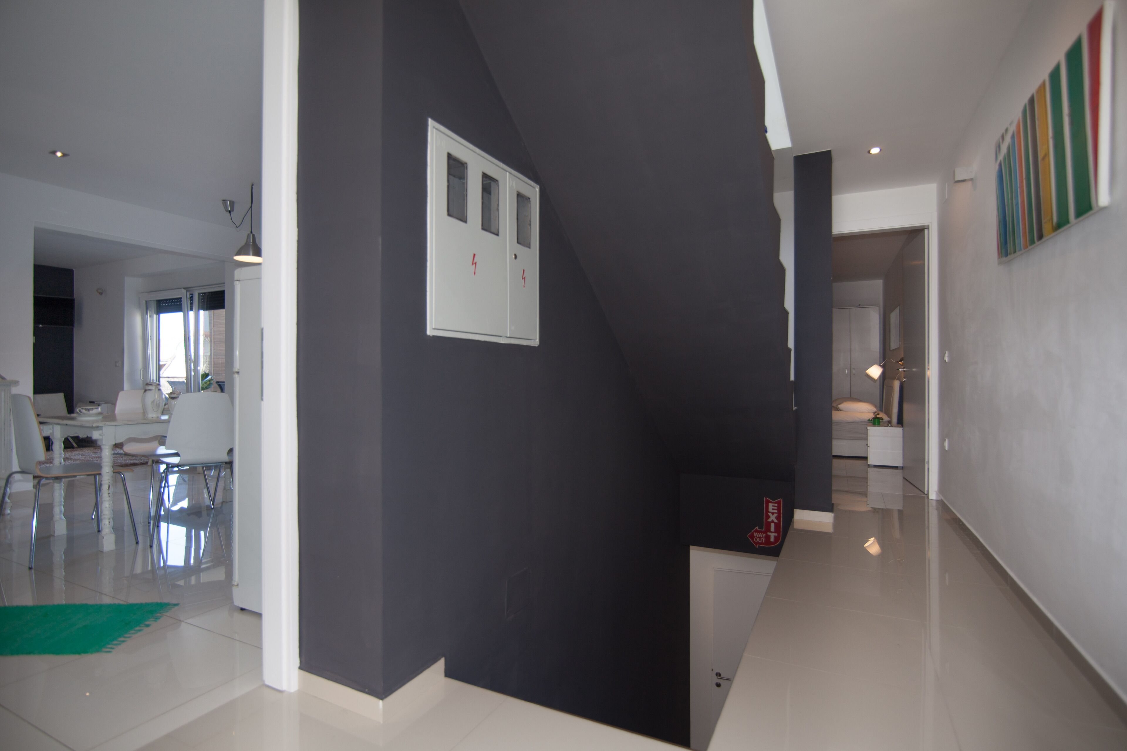 A modern interior with a dark accent wall, a staircase, and a dining area with chairs and a table.