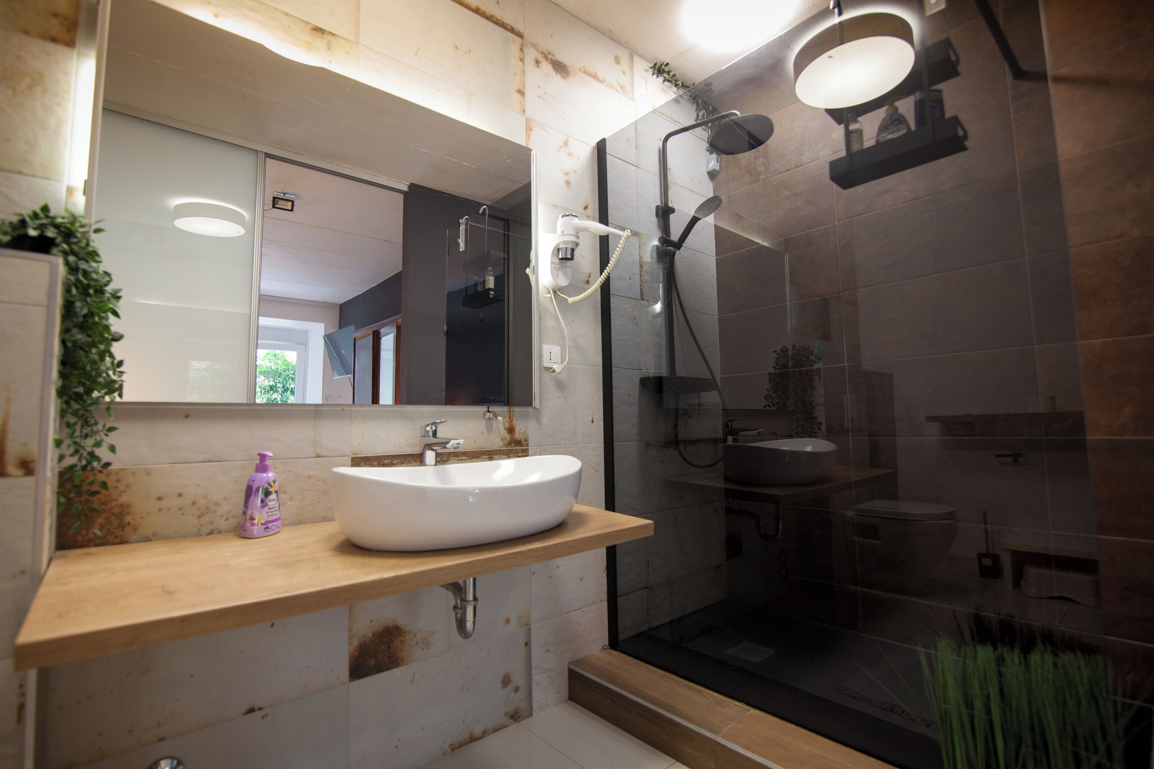 Ein modernes Badezimmer mit Waschbecken, Holzkommode und einer Duschkabine aus Glas.