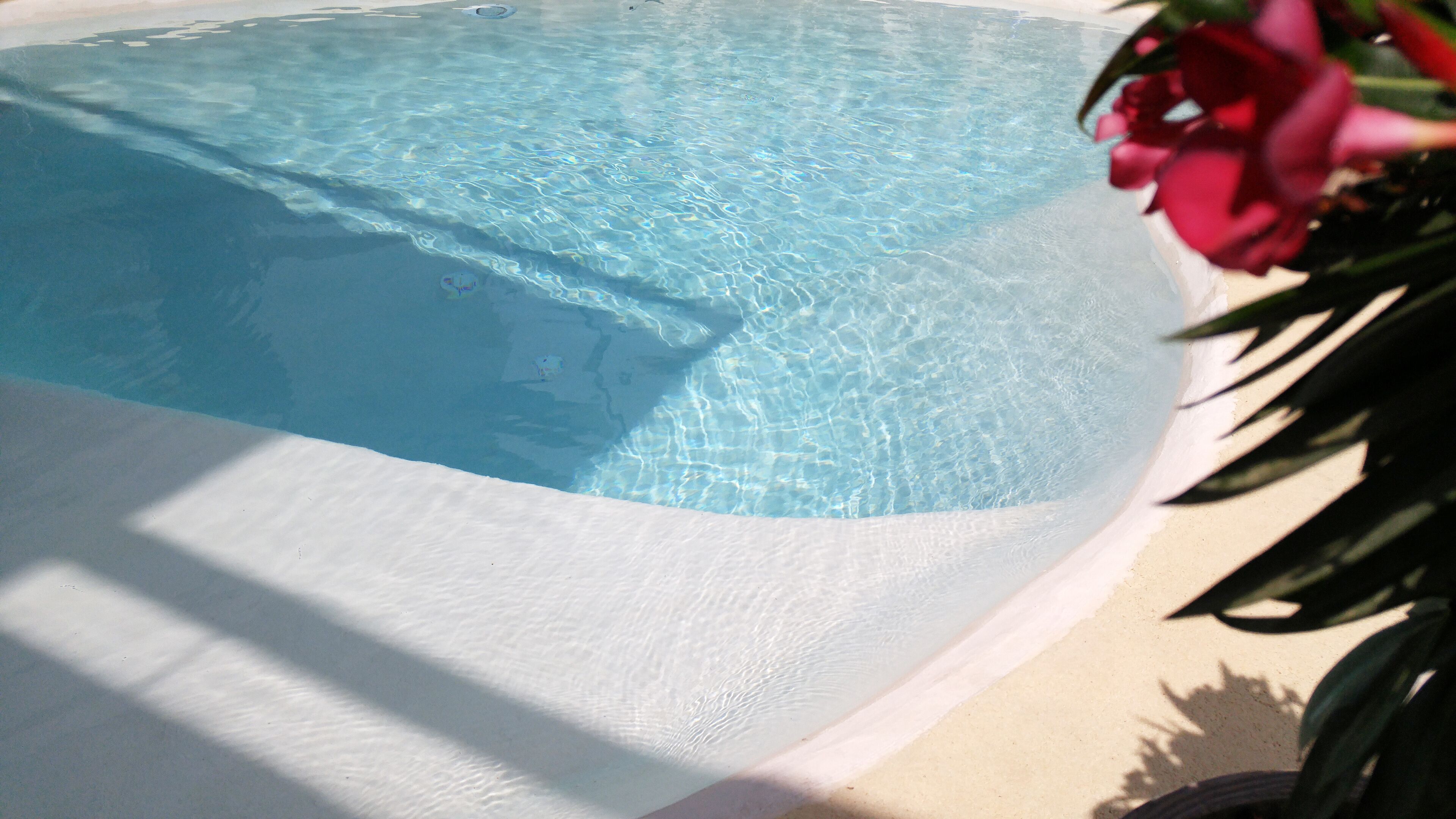 Piscina translúcida com borda branca, rodeada por um deck de cor clara.