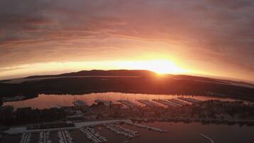 An aerial view of a marina with boats docked, surrounded by hills and a sunset.