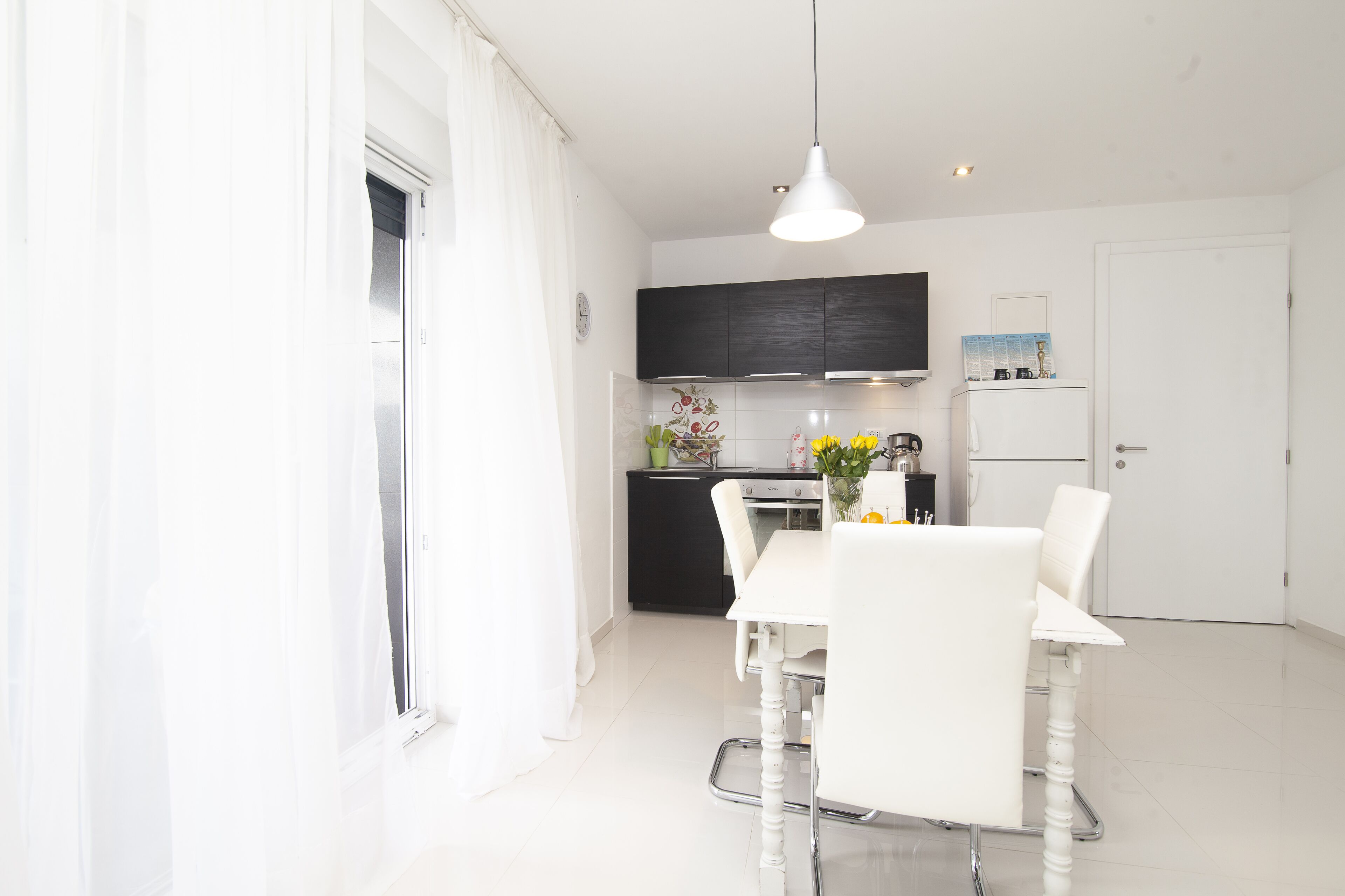 A modern kitchen with white cabinets, a black countertop, and a dining area with a white table and chairs.