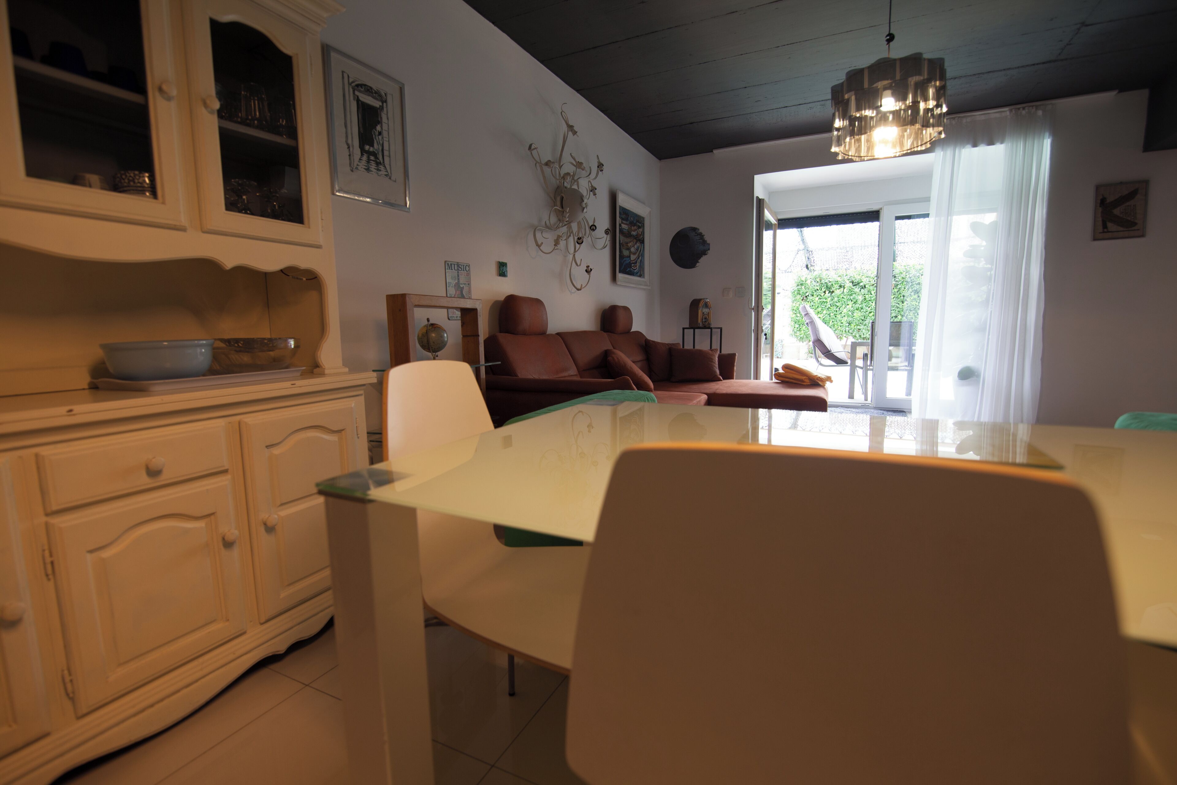 Et spiseområde med et glasbord og stole, et hvidt skab med skuffer og en brun sofa.