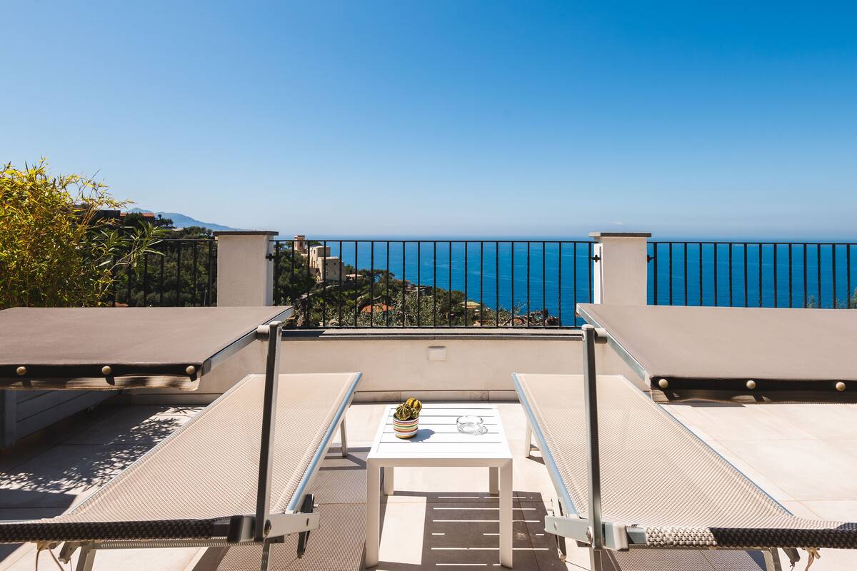 Eine Dachterrasse mit Liegestühlen, einem Tisch und Blick aufs Meer.