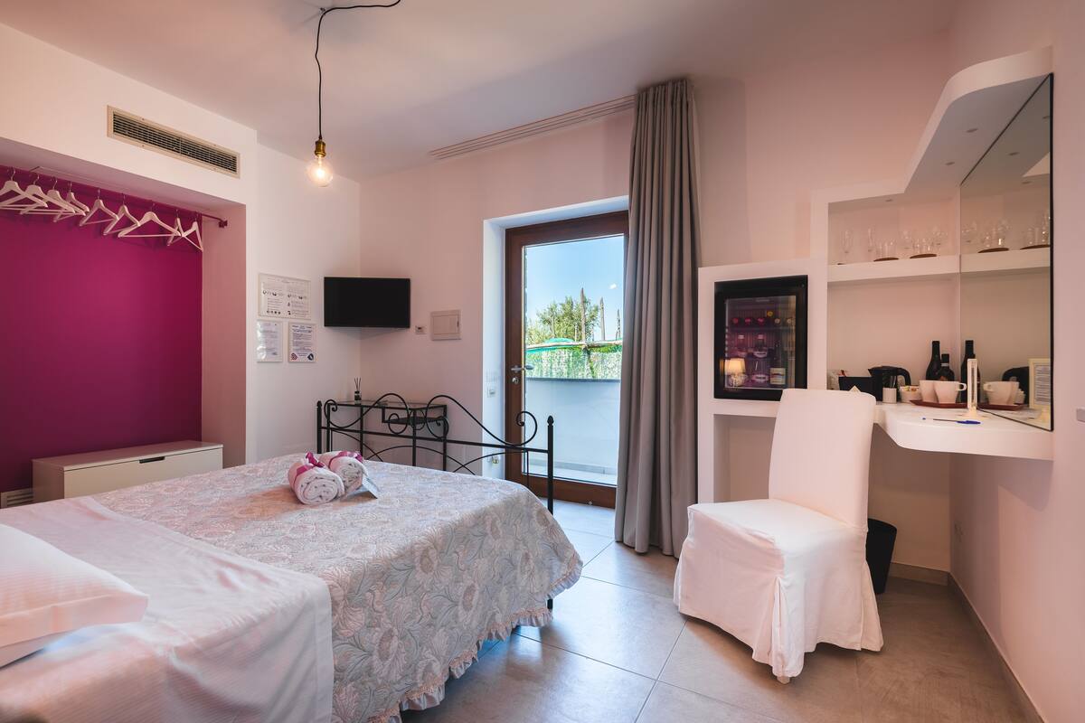 Ein Schlafzimmer mit Bett, Stuhl, Schreibtisch, Fernseher und einem Balkon mit Blick.