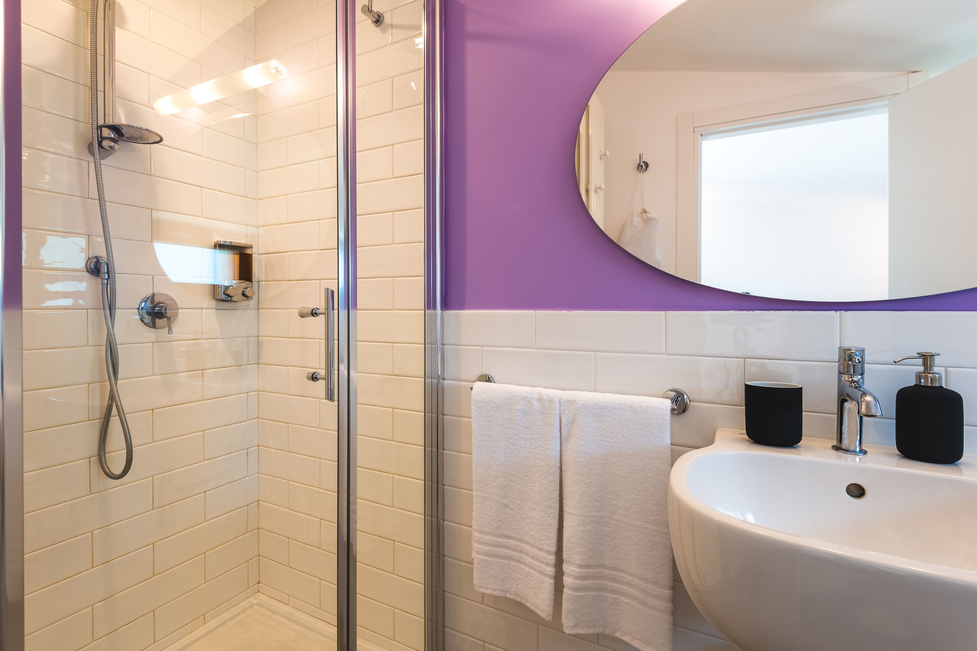 A bathroom with a glass shower enclosure, a white sink with a mirror above it, and a purple wall.