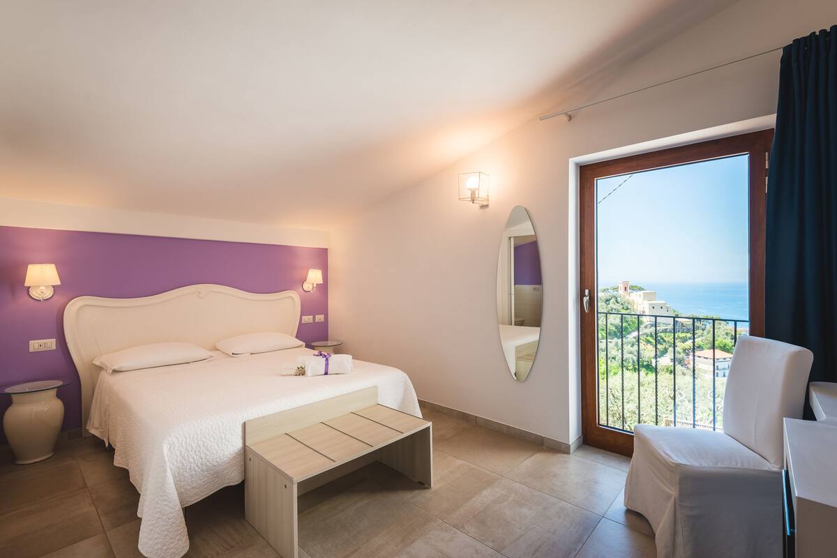 Ein Schlafzimmer mit Bett, Nachttischen, einem Spiegel und einem Balkon mit Aussicht.