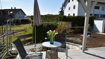 Eine Terrasse mit einem runden Tisch, zwei Stühlen, einer Blumenvase und einer Pergola.