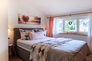 A bedroom with a bed, a window with curtains, a wall-mounted picture, and a nightstand.