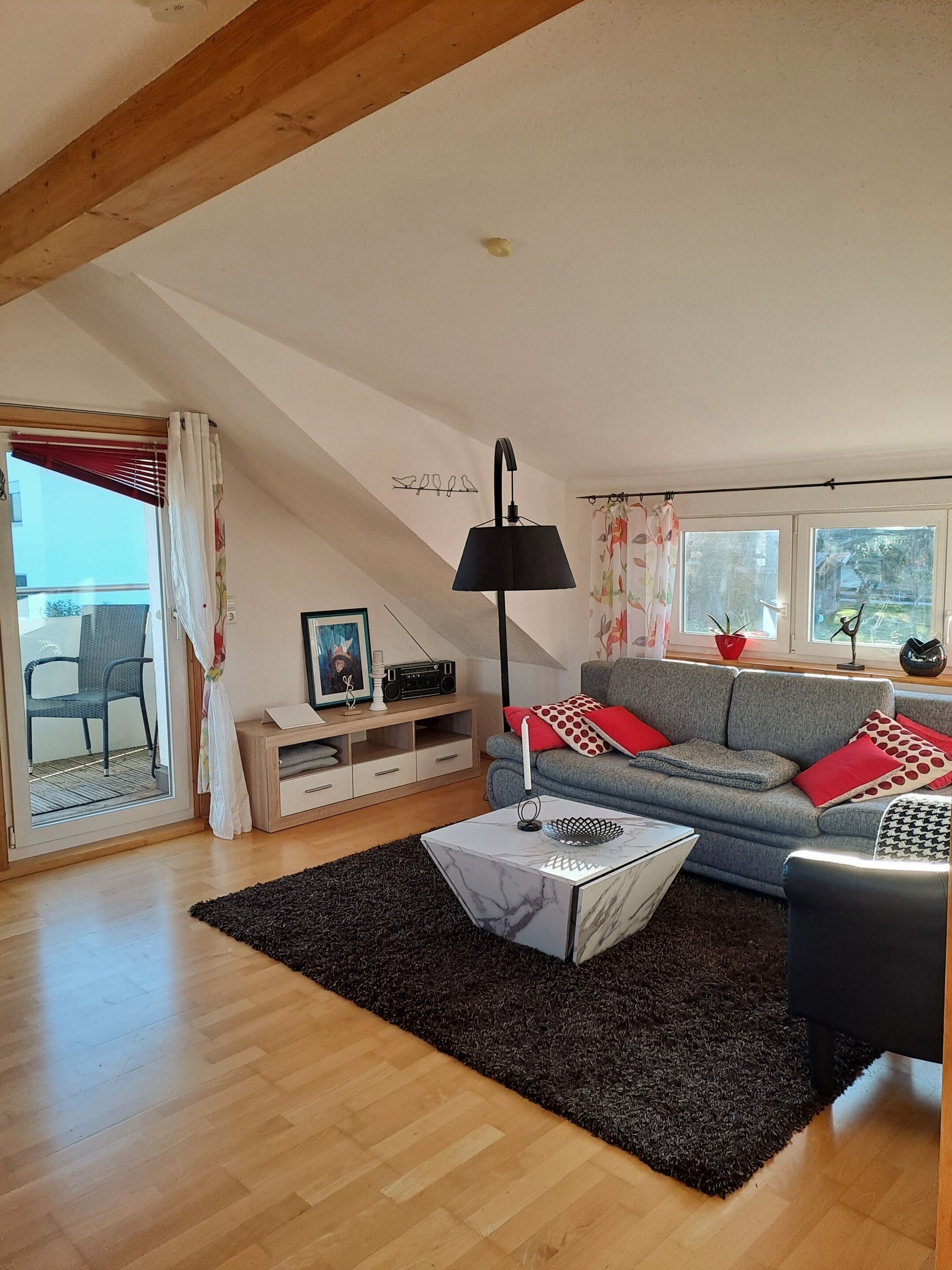 Ein Wohnzimmer mit Sofa, Couchtisch, Lampe, TV-Schrank und einem Fenster mit Vorhängen.