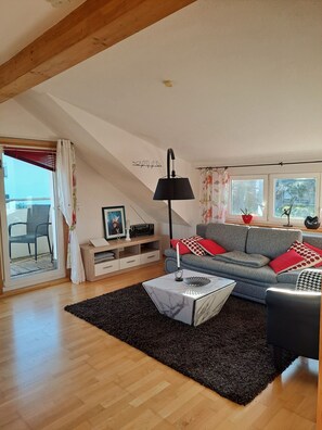 A living room with a sofa, a coffee table, a lamp, a TV stand, and a window with curtains.