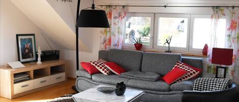 Ein modernes Wohnzimmer mit einem grauen Sofa, roten und weißen Kissen mit Muster, einem schwarzen Sessel, einem weißen Couchtisch und einer schwarzen Stehlampe.