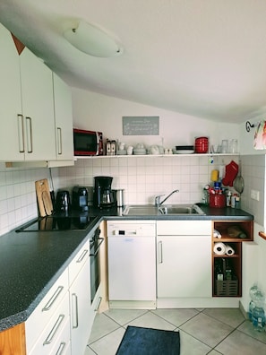A kitchen with white cabinets, a black countertop, a microwave, a coffee maker, and a dishwasher. - Apartment Bergblick - Countryside View (Hergatz)