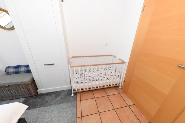 Une pièce avec un berceau blanc, une porte en bois et un tapis gris.