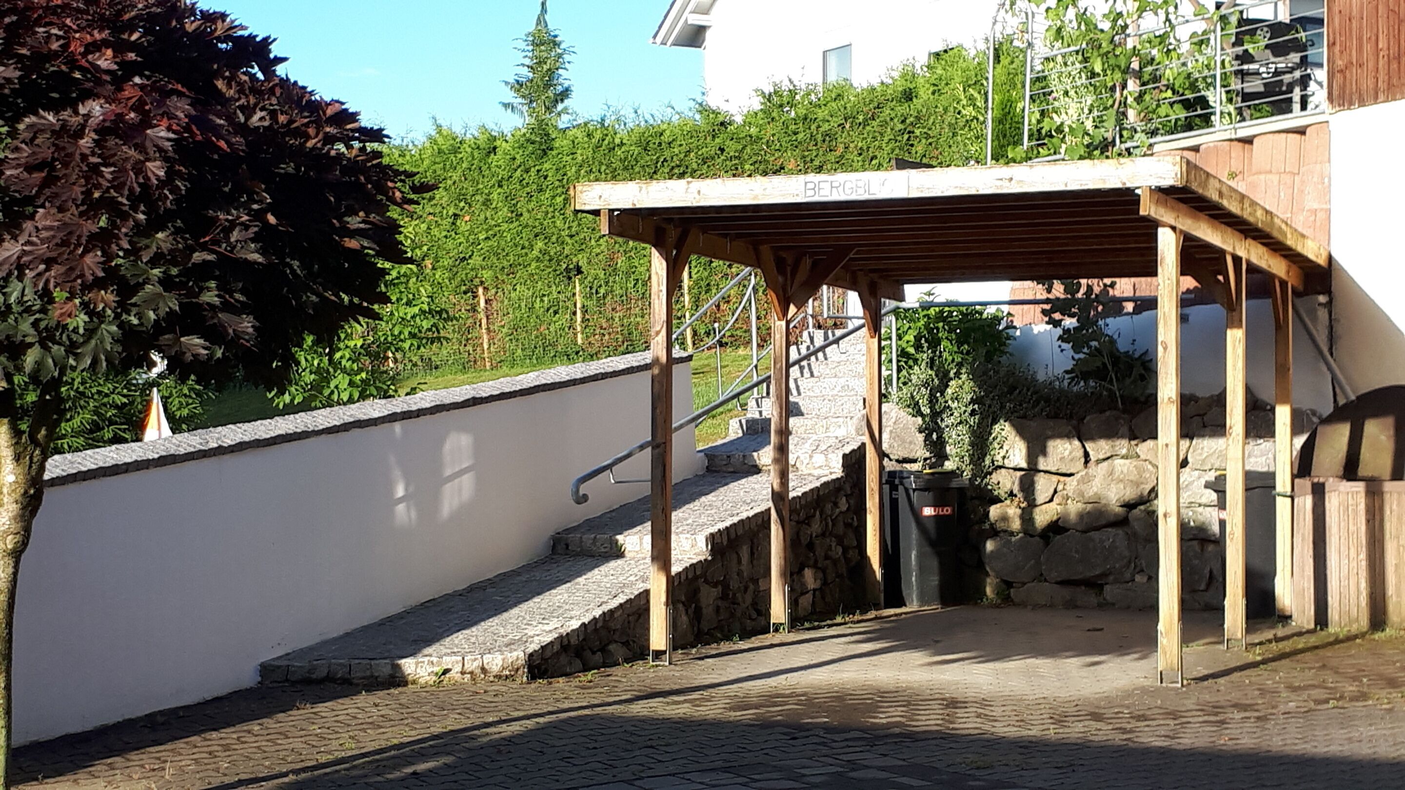 A stone staircase leading to a wooden pergola with a metal railing.