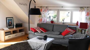 Ein modernes Wohnzimmer mit einem grauen Sofa, roten und weißen Kissen mit Muster, einem schwarzen Sessel, einem weißen Couchtisch und einer schwarzen Stehlampe.