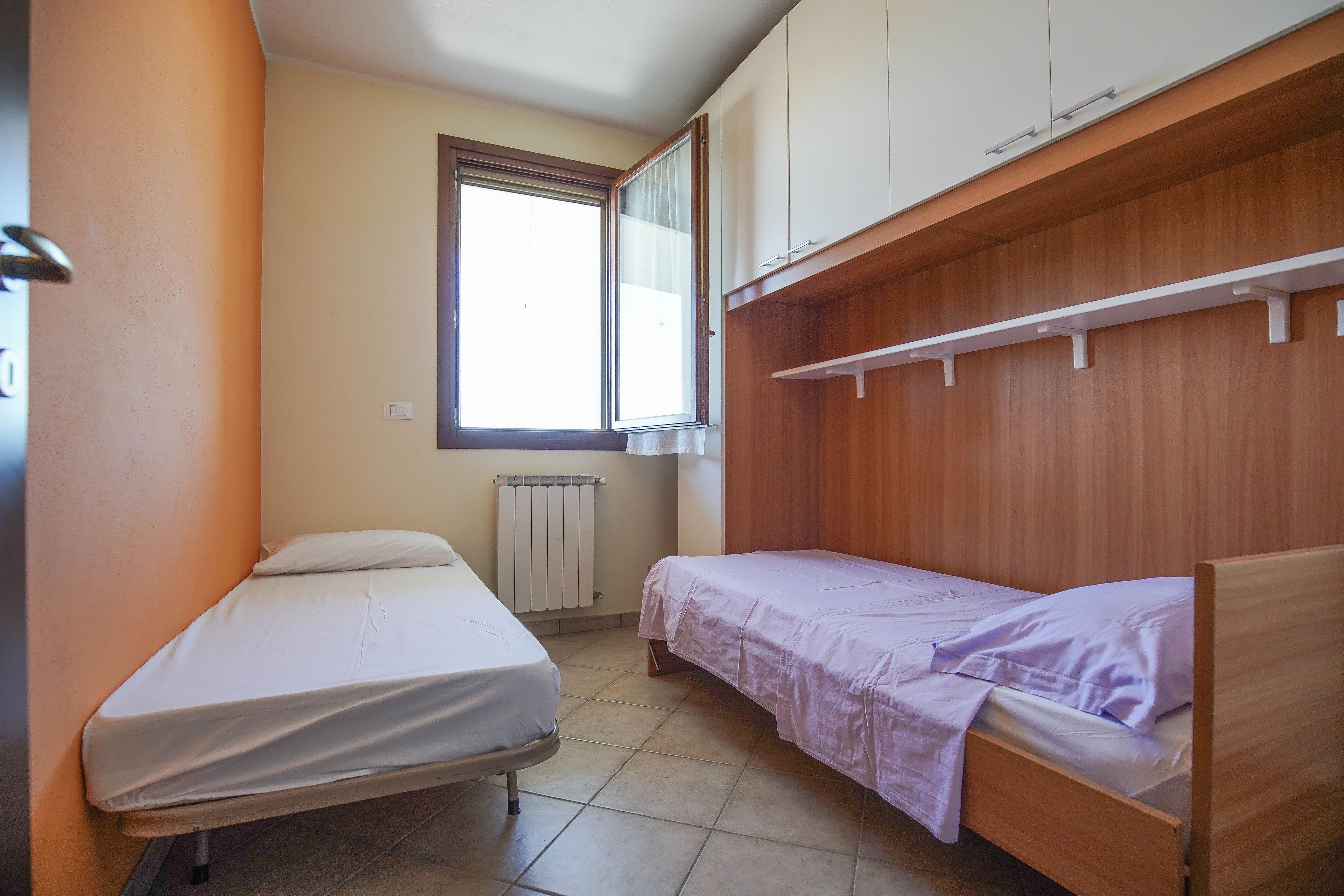 A small, single-bed room with a wooden wardrobe and a window with curtains.