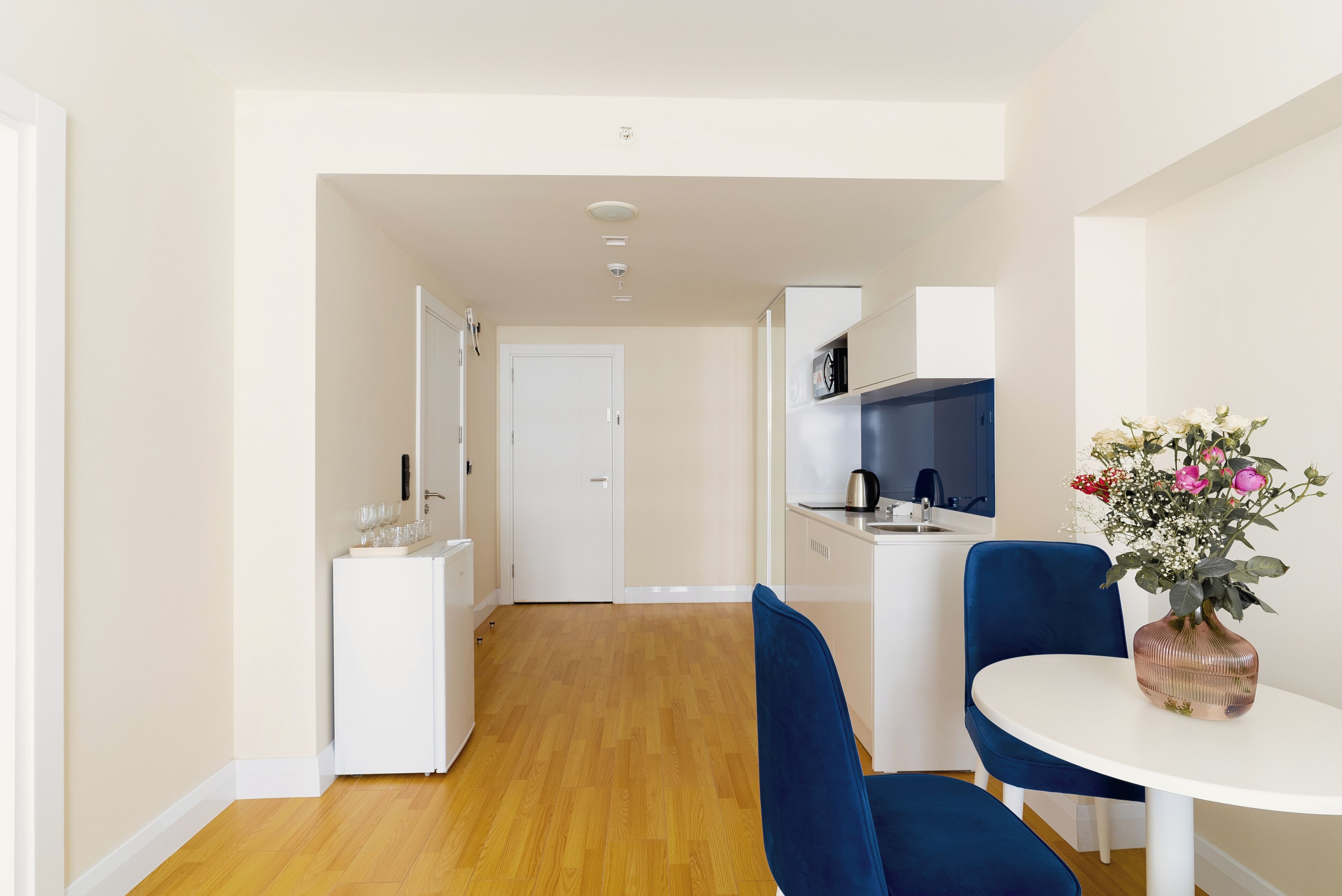 Una cocina moderna con armarios blancos, una silla azul y una mesa blanca con un florero.