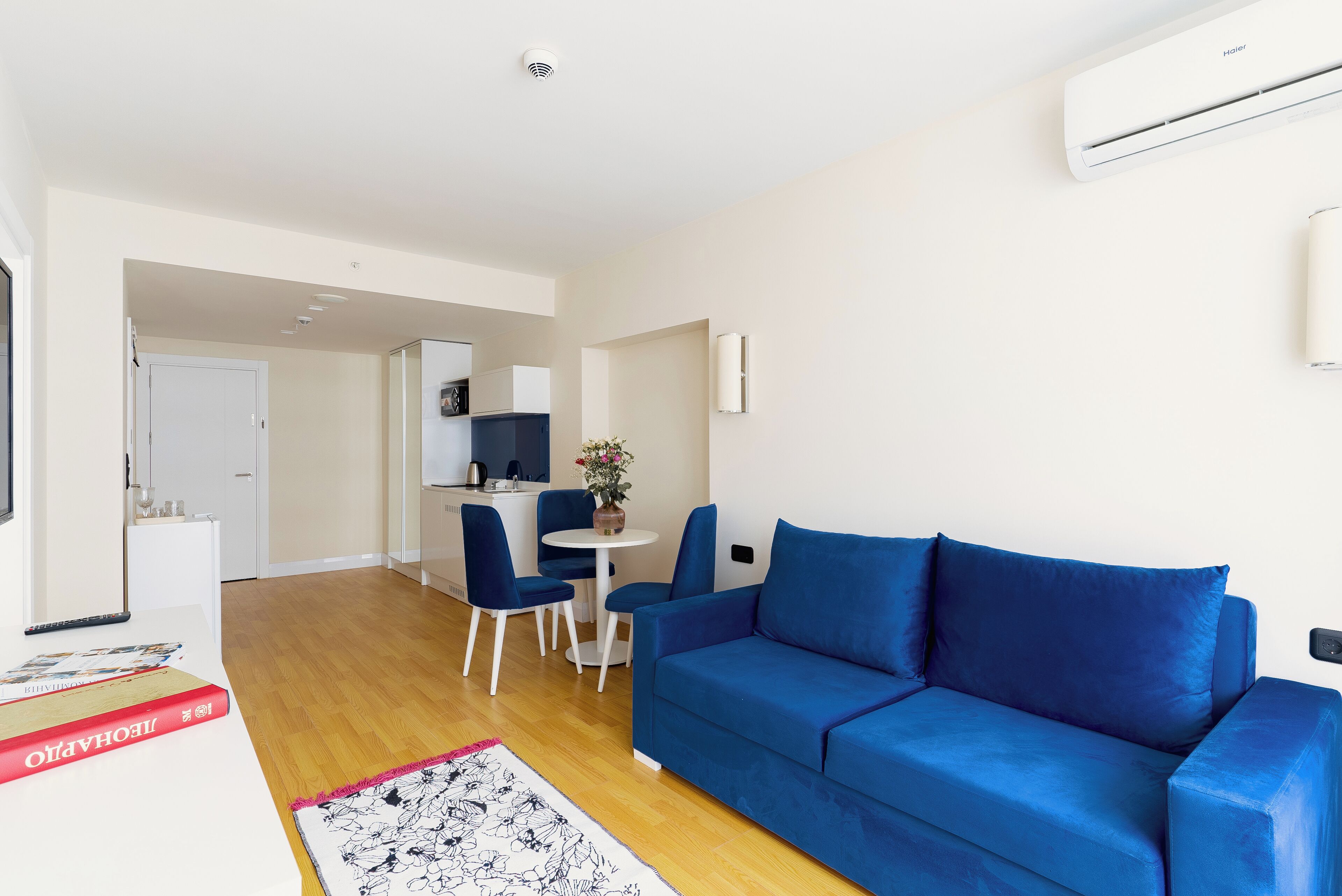 Een moderne woonkamer met een blauwe bank, een eettafel met stoelen en een keuken in de achtergrond.