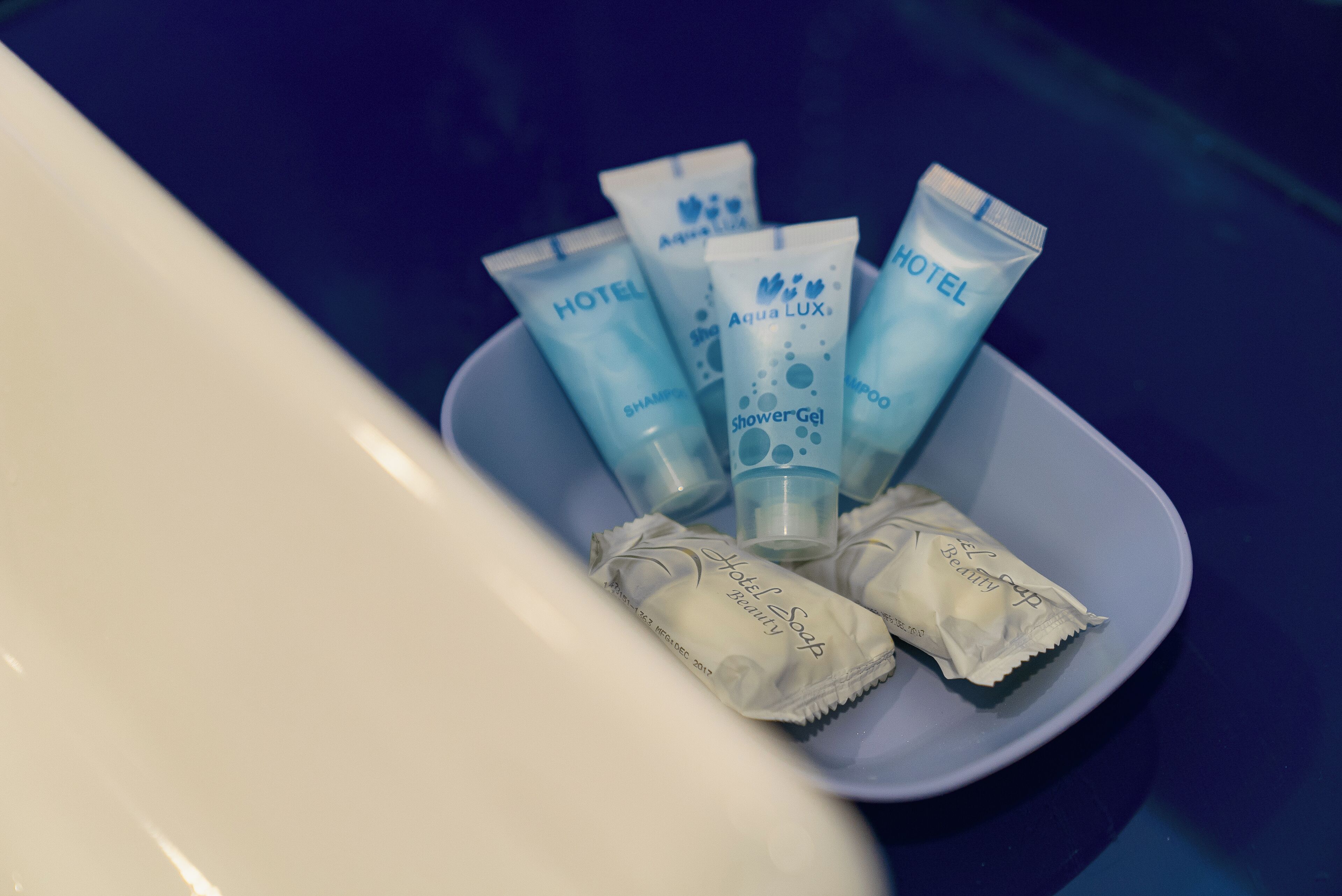 A bowl containing hotel toiletries including a shampoo, shower gel, and body soap.