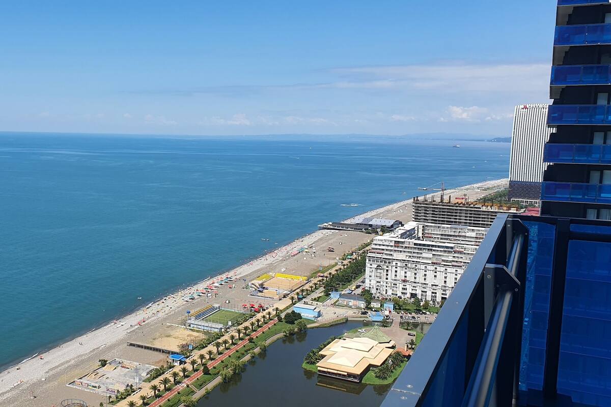 Un paisaje urbano costero con una playa, un puerto deportivo y rascacielos.