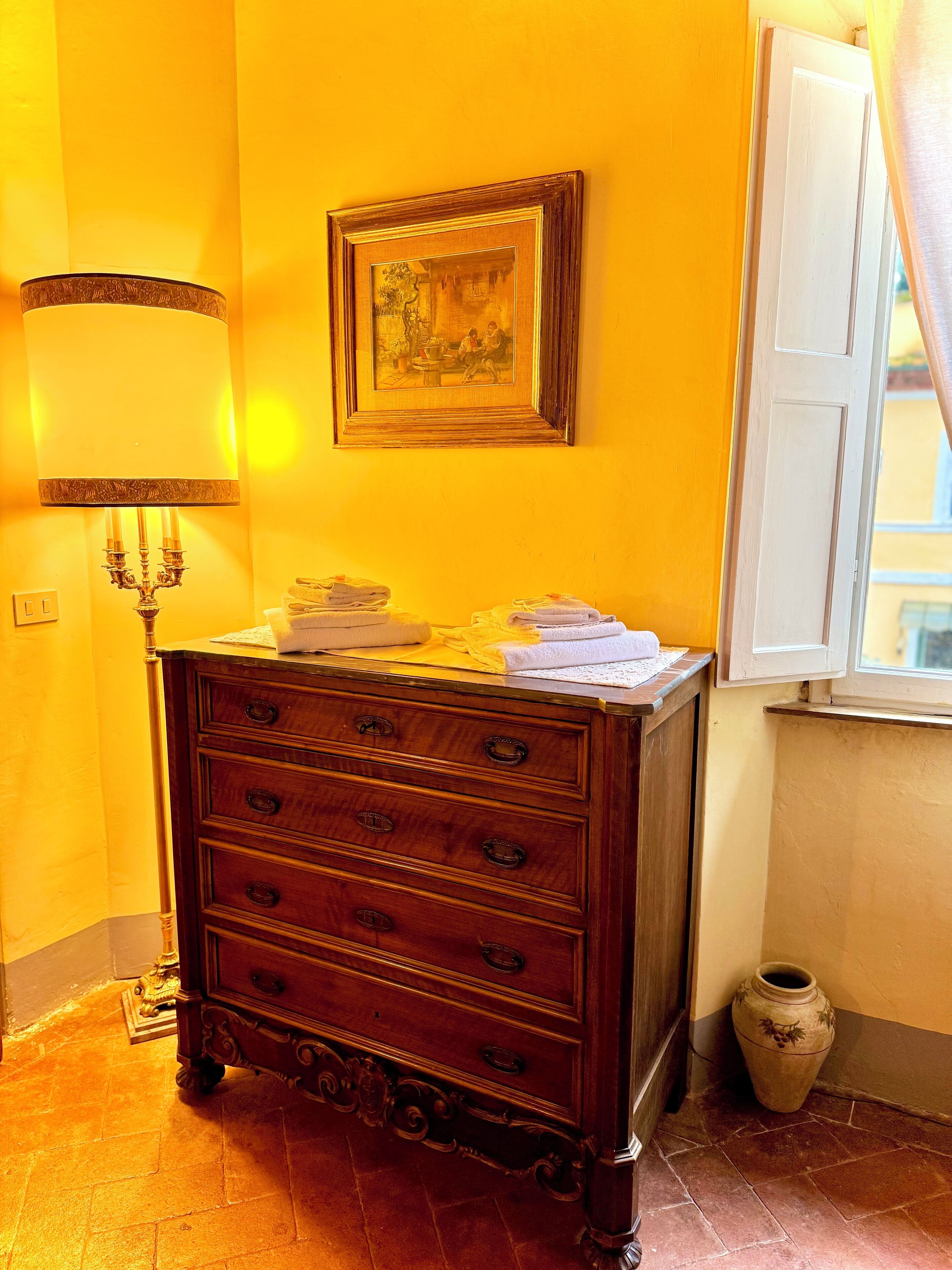 A wooden dresser with drawers, a framed picture on the wall, a lamp, and a window with curtains.