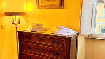A wooden dresser with drawers, a framed picture on the wall, a lamp, and a window with curtains.