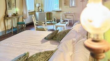 A bedroom with a wooden ceiling, a bed with white linens, a green upholstered chair, a small table, and a mirror on the wall.