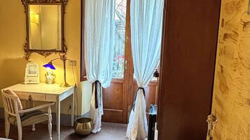 Quarto com cama, escrivaninha com luminária, espelho e janela com cortinas.