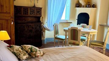 A bedroom with a large bed, a wooden dresser, a desk with chairs, and a fireplace.