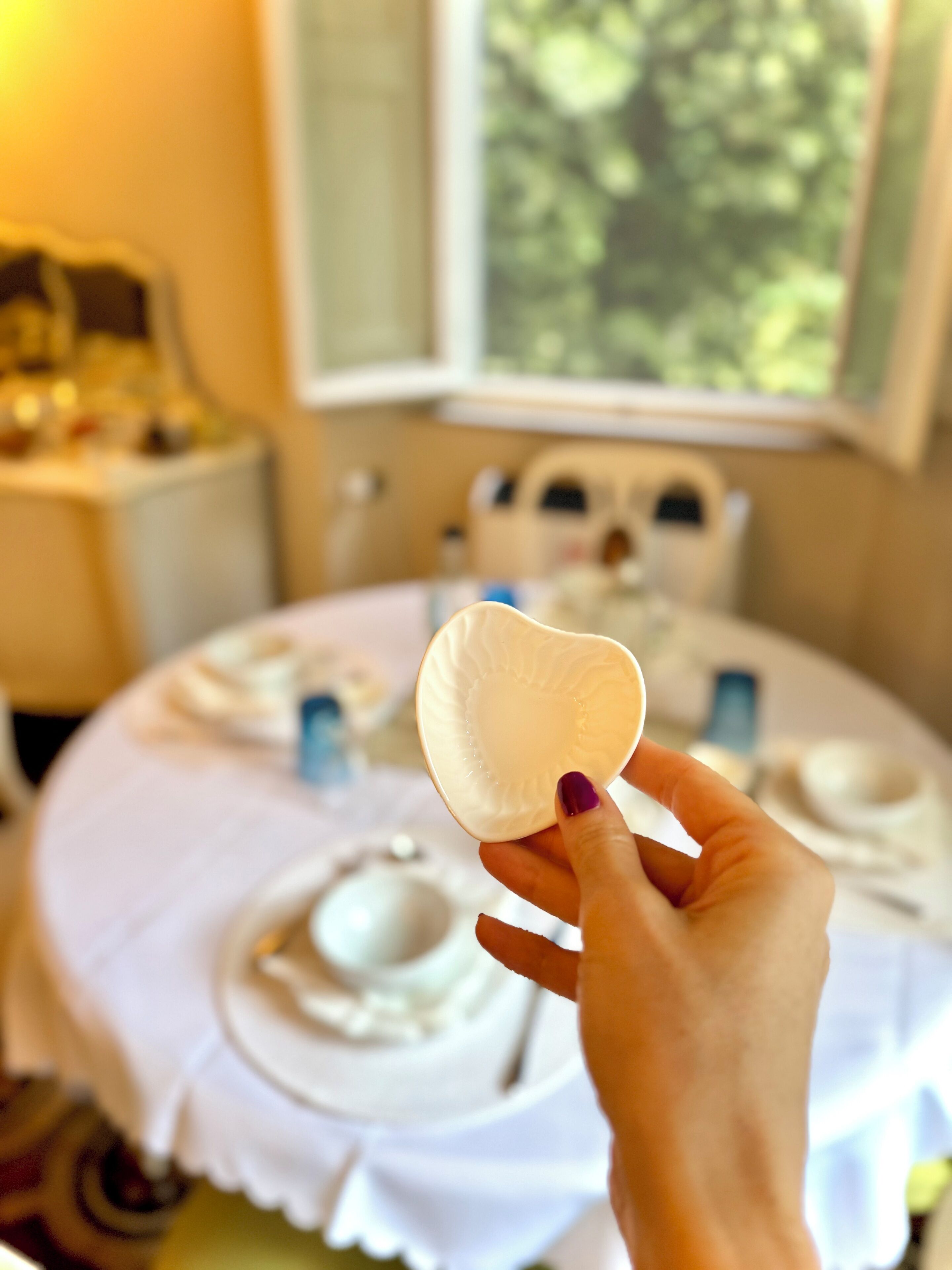 Une main tenant une assiette en papier blanche devant une table où se trouve de la vaisselle blanche.