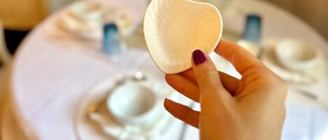 Une main tenant une assiette en papier blanche devant une table où se trouve de la vaisselle blanche.