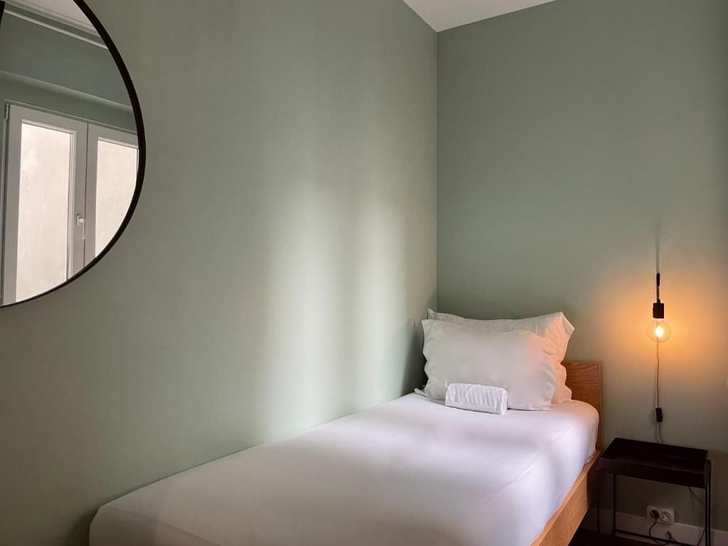 A single bed with white bedding in a room with light green walls.