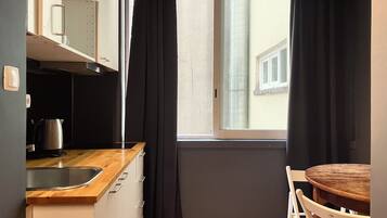 Een kleine keuken met raam, een spoelbak, waterkoker en een houten tafel met stoelen.