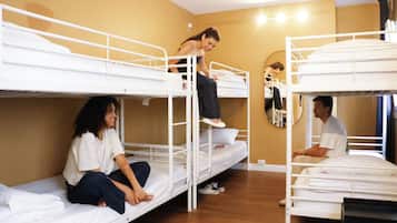 A dormitory room with bunk beds, a mirror, and a wooden floor.