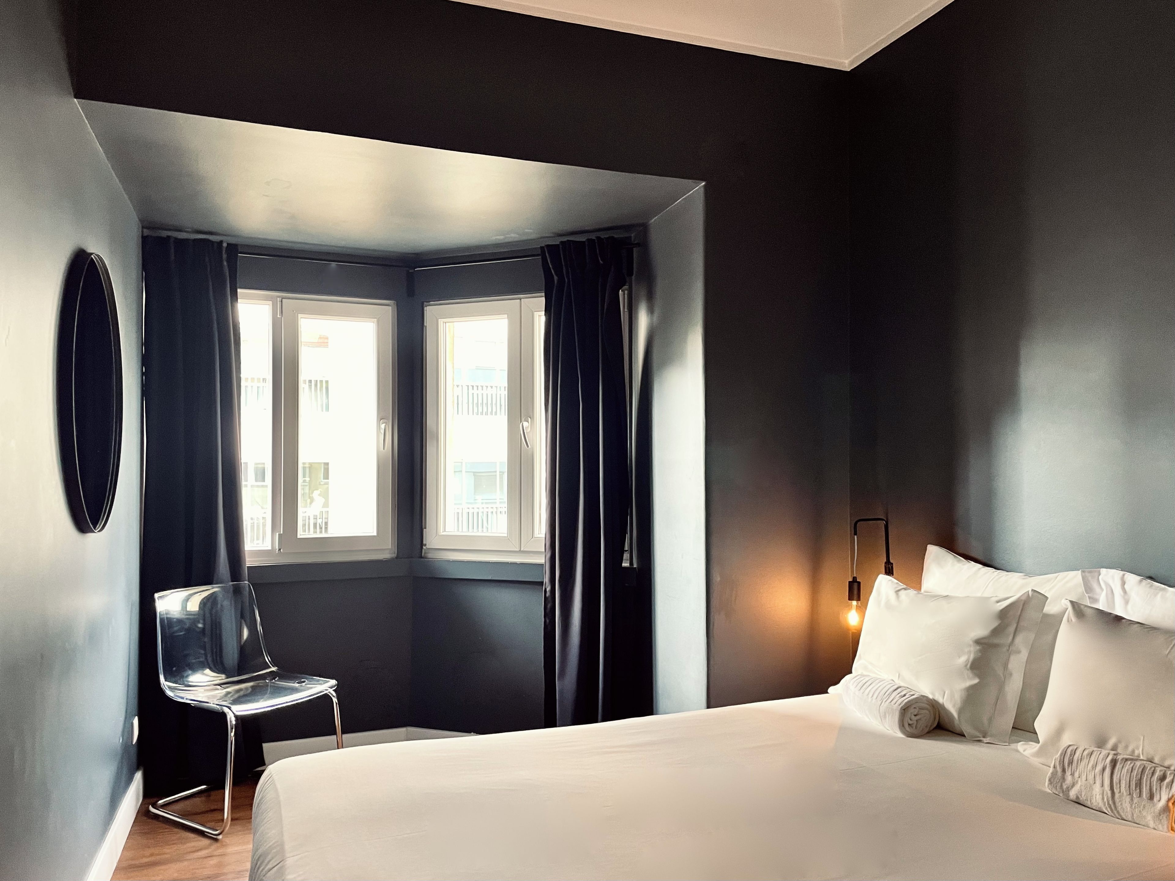 Een hotelkamer met een bed, een stoel, een raam met gordijnen en een wandlamp.