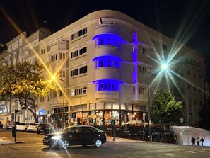 Un hôtel à plusieurs étages, doté d’une façade incurvée illuminée de lumières bleues et jaunes, et d’un café situé au rez-de-chaussée.