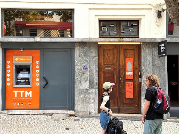 A storefront with a TTM Express ATM, a wooden door, and a sign that reads 'TALK TO ME.' - Avenue Rooms & Suites - Hostel (Lisbon)