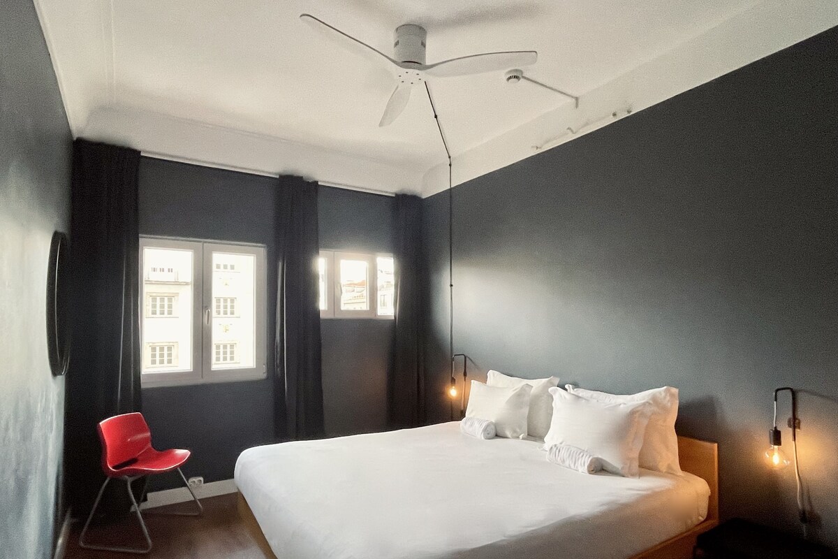 A modern bedroom with a large bed, a ceiling fan, and two wall-mounted lights.