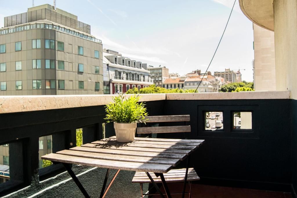 Un balcón con una mesa de madera y una planta en maceta, con vistas a un paisaje urbano con edificios modernos.