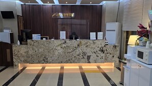 Ein Hotel-Rezeptionsbereich mit Marmor-Theke, einem digitalen Bildschirm und einem Schild mit dem Hotelnamen.