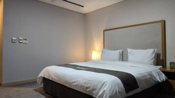 A hotel room with a large bed, a nightstand, a wall-mounted air conditioning unit, and a light fixture.