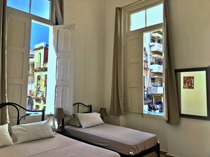 Una habitación con dos camas, una ventana que ofrece vistas a edificios y un cuadro enmarcado en la pared.