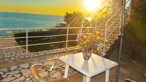 A patio with a table and chairs, a vase of flowers, and a view of the sea.