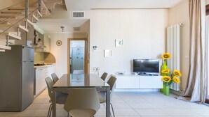 Una cocina moderna con un refrigerador empotrado, una mesa de comedor con sillas, un televisor y un florero con girasoles.