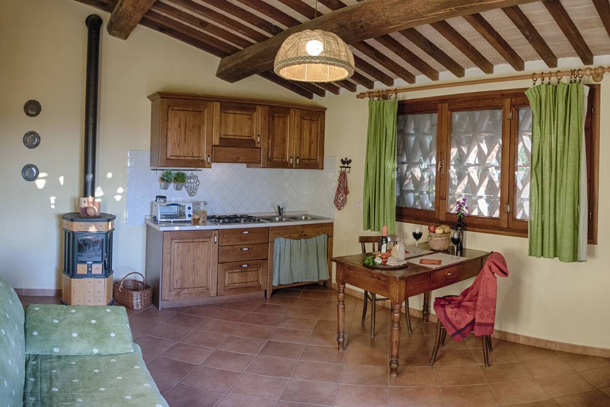 A cozy kitchen with wooden cabinets, a dining table, and a window with green curtains.