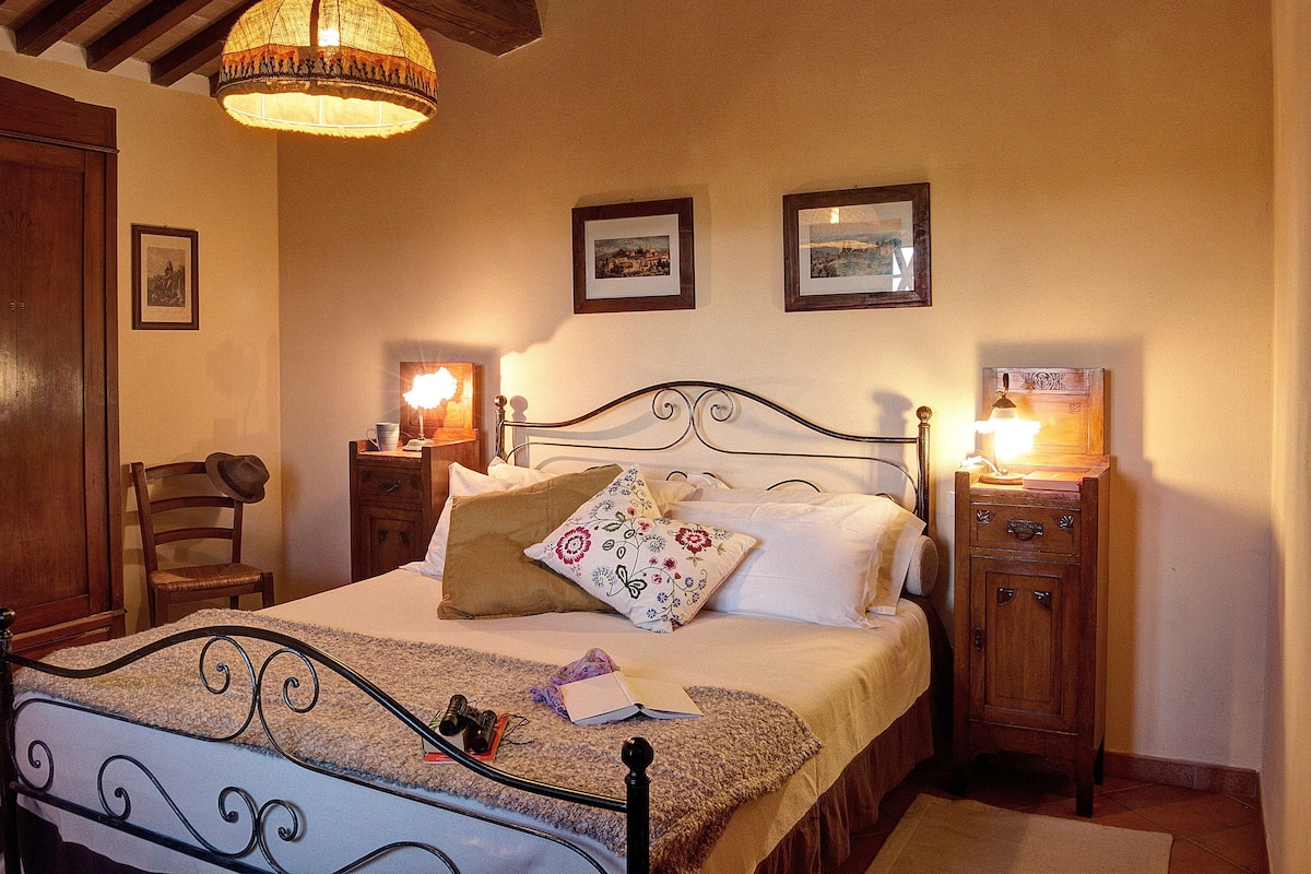 A neatly arranged bedroom with a bed, bedside tables, a chair, and a hanging light fixture.